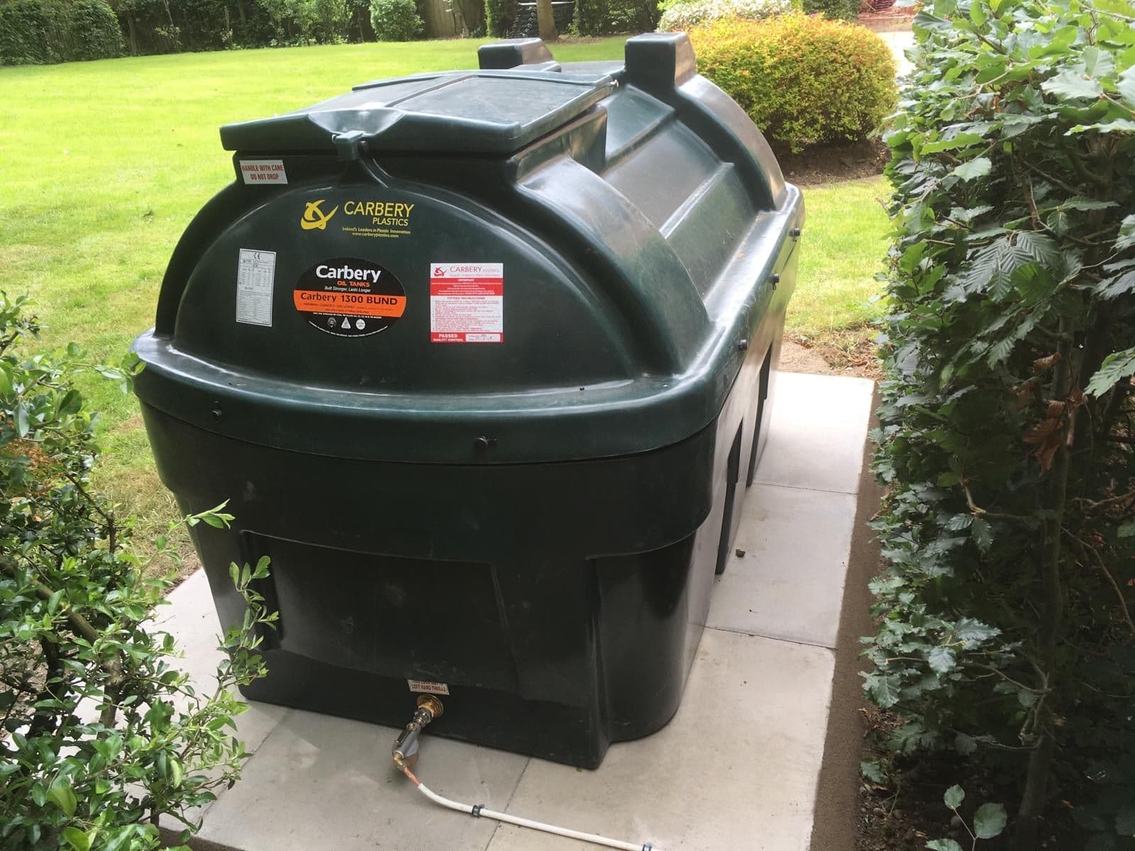 A Carbery 1300 litre bunded oil tank on a paved base, with the outlet valve, filter and oil line visible at the bottom of the tank