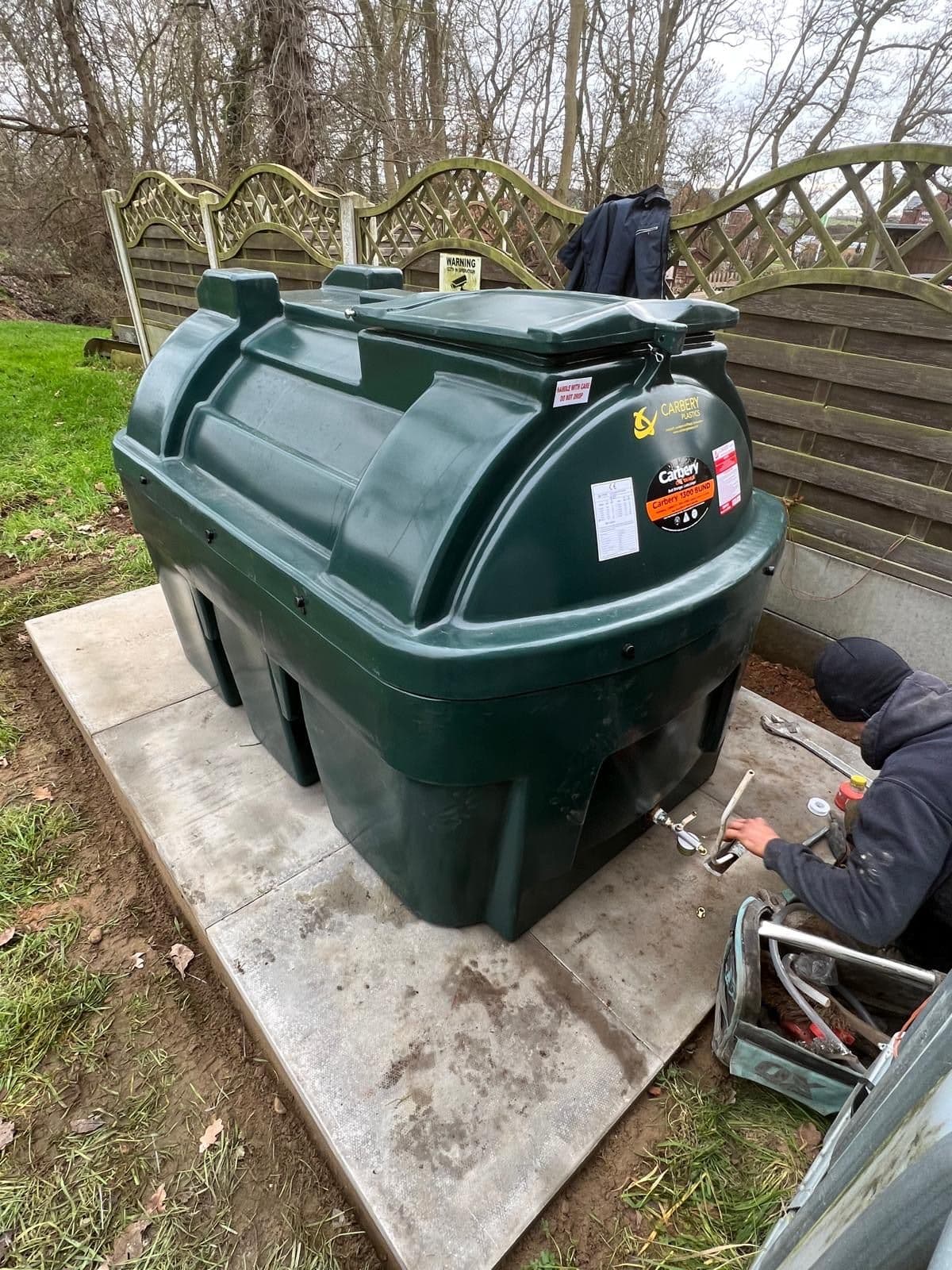 An engineer working on the outlet fittings at the base of a green bunded oil tank, drawing fuel off into a container