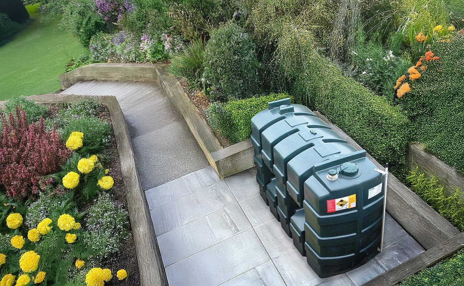 A green Titan bunded oil tank installed on a paved base in a landscaped garden, set into a planted border beside a lawn